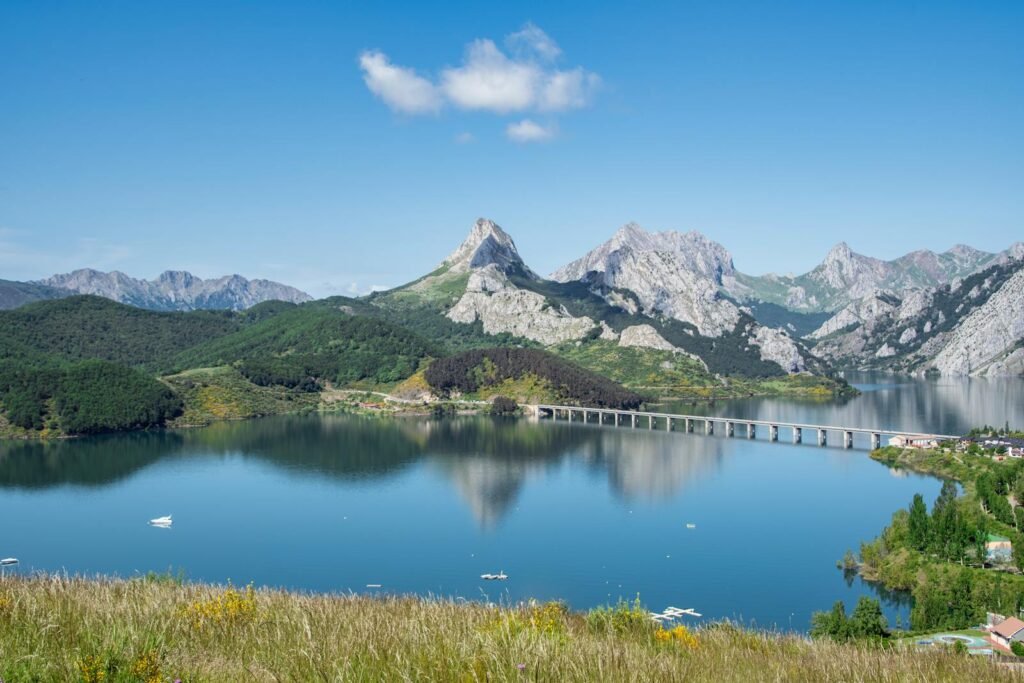 Beautiful mountain landscape with a lake and bridge reflecting in the water under a clear blue sky.